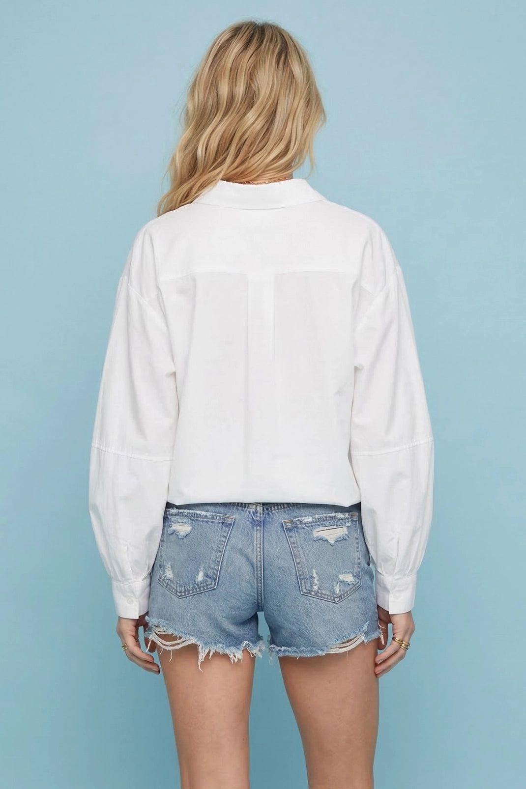 Back view of a model wearing the white balloon sleeve blouse with denim shorts.